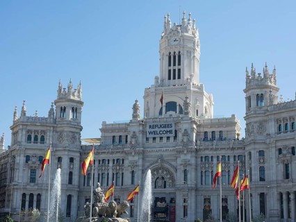 Monumental white palace with Spanish flags, spring fountain and a welcome banner for refugees,