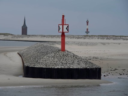 Red beacon on gravel embankment, church tower and lighthouse in the background, sand dunes and grey