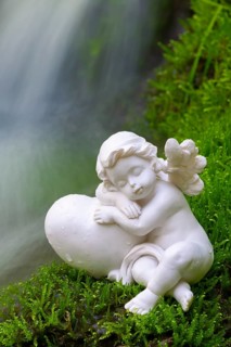 Porcelain angel figurine on moss by a waterfall