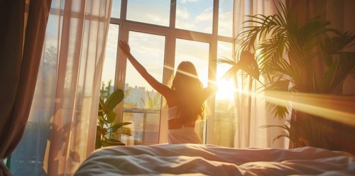 A woman is in bed, smiling and stretching her arms after waking up at sunrise early morning, AI