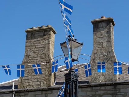 Stone houses in the village, decorated with blue and white flags and an old street lamp, grey