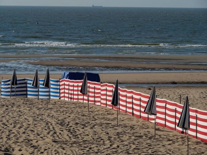 Wide sandy beach area with scattered blue and white striped and black umbrellas and the sea with