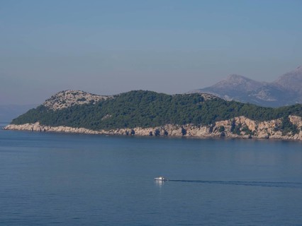 A small boat sails on the calm sea along a forested chain of islands, the old town of Dubrovnik