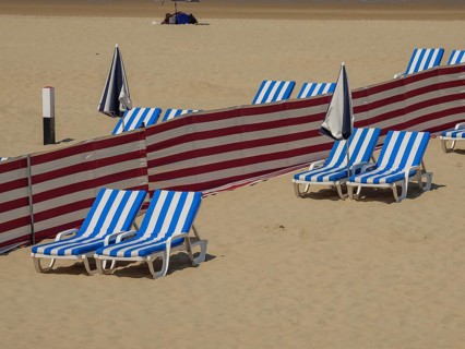 Beach where blue and white striped deckchairs, parasols and red partitions are arranged in rows,