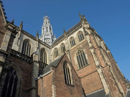 Historic Gothic church with high tower and ornate window facades under a clear sky, Haarlem,