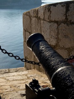 Close-up of a black cannon on an old stone wall overlooking the sea, the old town of Dubrovnik with