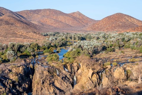 Kunene River with green vegetation in dry red mountain landscape, waterfall and African Baobab