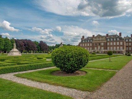 Symmetrical garden with manicured hedges and paths in front of a historic castle under a cloudy