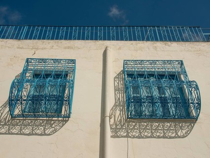 Decorative blue balconies on a white wall cast shadows, Tunis in Africa with ruins from Roman
