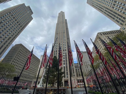 Tall skyscraper with several american flags in the foreground, surrounding tall buildings and
