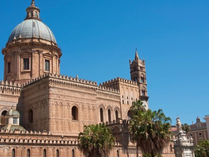 Historic cathedral with towers and a dome, surrounded by palm trees under a clear blue sky, palermo