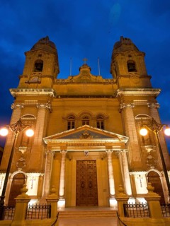 Illuminated church facade at night, with two towers, lamps and decorative elements, Valetta, Malta,