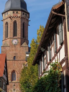 Stone church tower and half-timbered houses with autumn leaves under a blue sky, historic