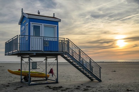 A blue and white rescue tower with a secured boat next to it, in front of an idyllic sunset on the
