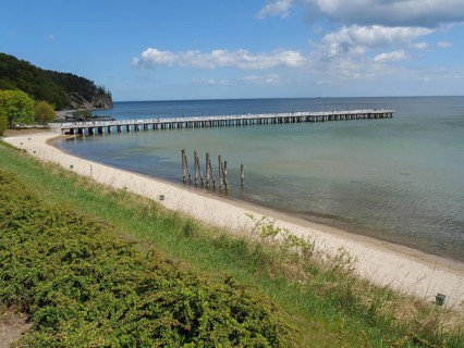 A sandy beach with a jetty leading into the sea, green coast and cloudy sky in the background,