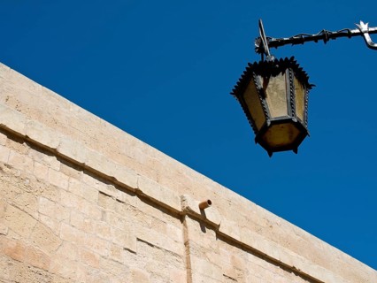 An ancient lantern hangs on a stone wall against a deep blue sky, the town of mdina on the island