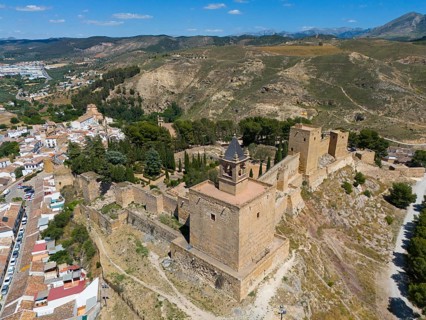 Historic castle complex on a hill in a mountainous area of Spain, surrounded by vegetation in sunny