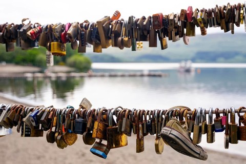 Many love locks on a railing with a lake and mountains in the background