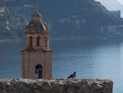 A bell tower with a dove in the foreground, the sea and mountains in the background, a peaceful