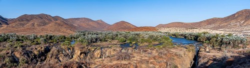 Panorama, Kunene River with green vegetation in dry red mountain landscape, waterfall and African