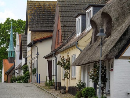 Traditional houses with thatched roofs and a pointed tower at the end of the street, along a quiet,