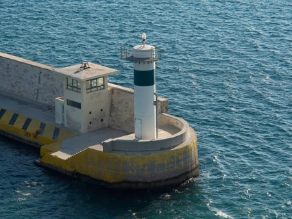 A lighthouse at a harbour surrounded by blue water in daylight, Ancient buildings with columns and