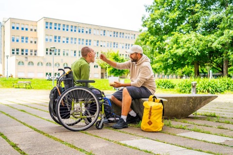 Full length photo of a caucasian adult college student feeding a friend with cerebral palsy on