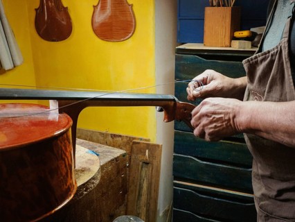 Craftsman stringing a musical instrument, possibly a violin, in a traditional workshop