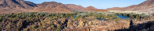 Panorama, Kunene River with green vegetation in dry red mountain landscape, waterfall and African