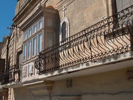 Facade of an old building with wrought iron balcony railings and a cross on a niche, the island of
