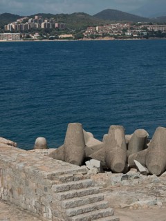 Coastline with concrete breakwaters and a view over the sea to a town and hills, Corsica, ajaccio,