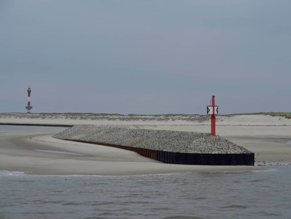Red beacon on a gravel embankment along the coast with sand dunes and grey sky, buhne on an island