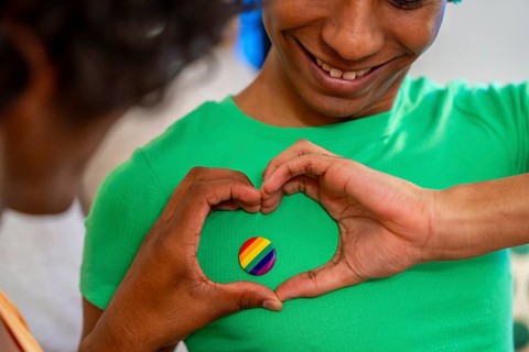 Gay man gesturing heart shape around LGBT badge next to his partner at home
