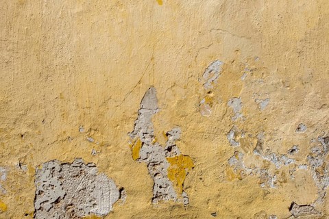 A weathered yellow wall with peeling paint and visible damage, Rhodes, Greece, Europe