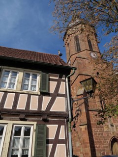 Traditional tower and half-timbered house surrounded by trees under a blue sky, historic