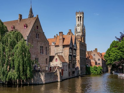 Historic buildings and a tall bell tower along a river on a sunny day, historic city by the river