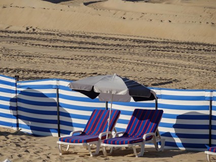 Blue and white striped deckchairs next to a parasol on the beach, bordered by blue and white