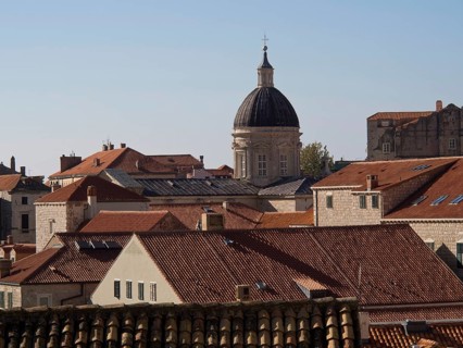 Historic buildings and a church with a dome surrounded by red tiled roofs under a clear blue sky,