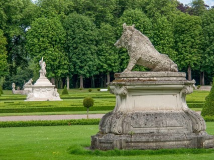 Stone sculpture of a boar in a spacious park with hedges and trees, historic castle with a green