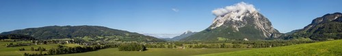 Meadows and fields in the morning light, behind the village of Irdning and the Grimming, panoramic
