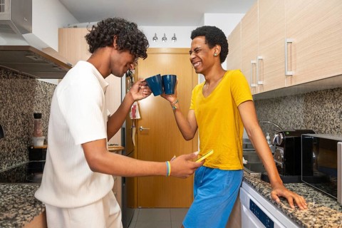 Happy gay couple enjoying coffee and looking at the mobile at home in the morning