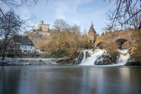 Beautiful landscape in winter with ice and snow. Waterfall of the river Elz near the castle