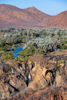 Kunene River with green vegetation in dry red mountain landscape, waterfall and African Baobab