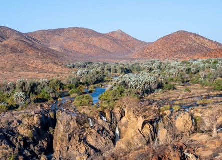 Kunene River with green vegetation in dry red mountain landscape, waterfall and African Baobab