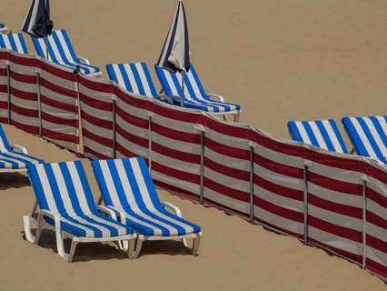 Close-up of blue and white striped deckchairs and umbrellas on clean sandy beach, colourful beach
