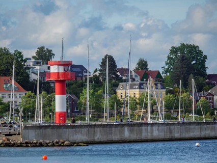 Red and white lighthouse and sailing boats along the coast against a background of trees and