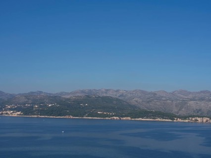 Tranquil coastal landscape with gentle mountains and clear blue skies reflected in the calm sea,