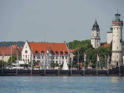 Town view with historical buildings, lighthouse and sailing boats on the calm water, towers at a