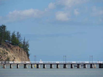 A pier next to a cliff with trees stretching into the sea under a cloudy sky, spring on the Baltic