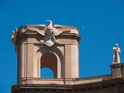 Close-up of a building tower decorated with sculptures and an eagle under a clear blue sky, palermo